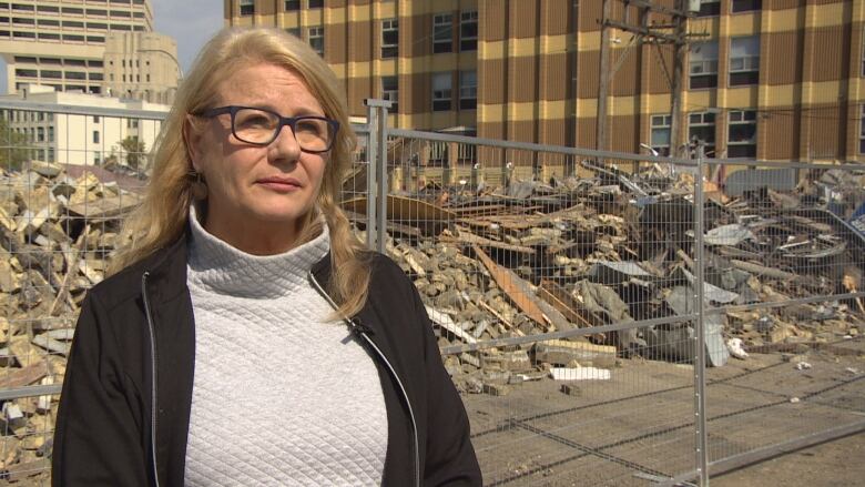 A women stands in front of a pile of debris.