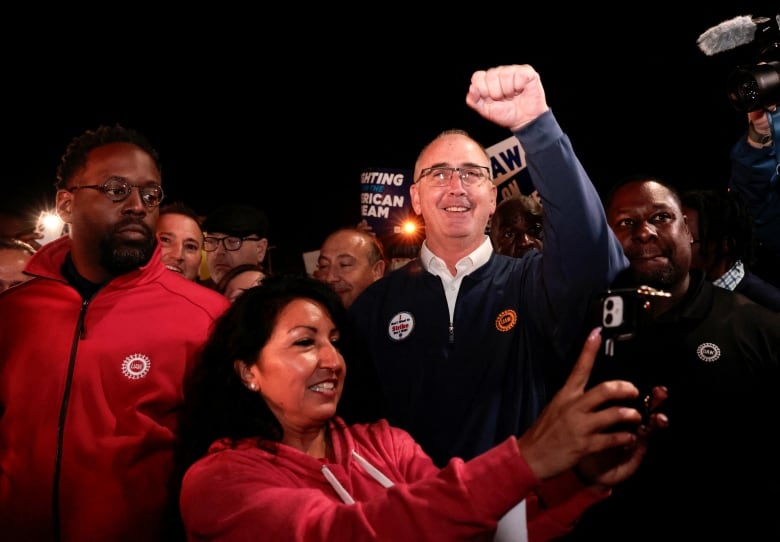 A man in a blue shirt raises his fist on a picket line.