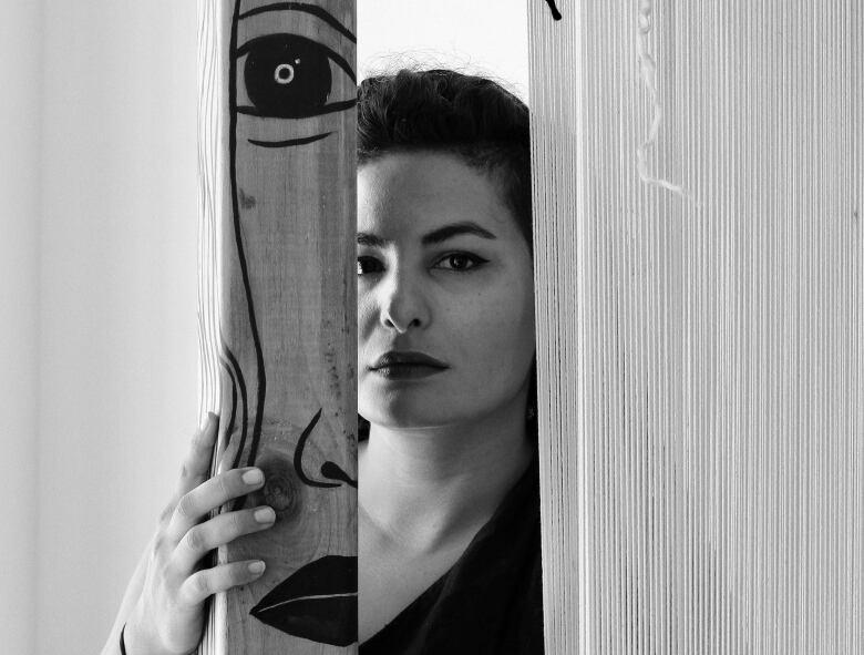 Black and white photo of a woman who's looking at the camera but half her face is obscured by a wooden post