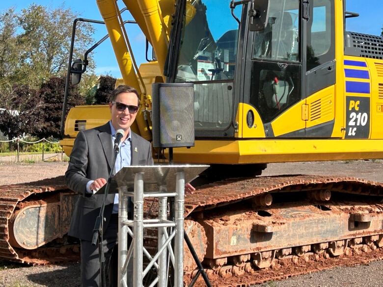 Dan Kucher at podium in front of a backhoe