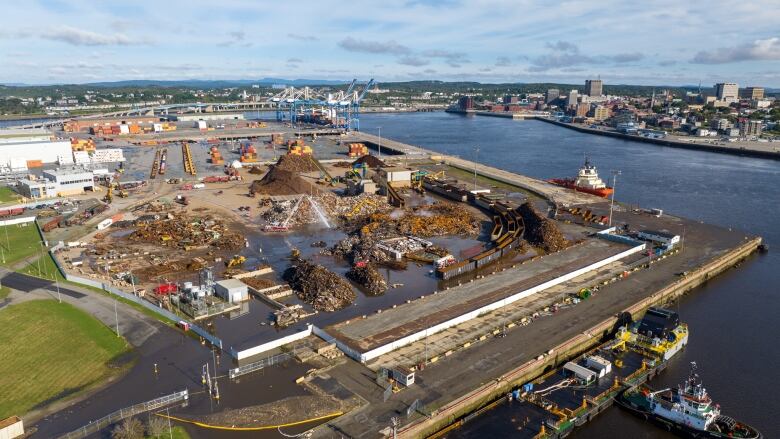 Areal shot of a scrap yard overlooking the harbour, showing fire trucks pouring liquid over charred metal