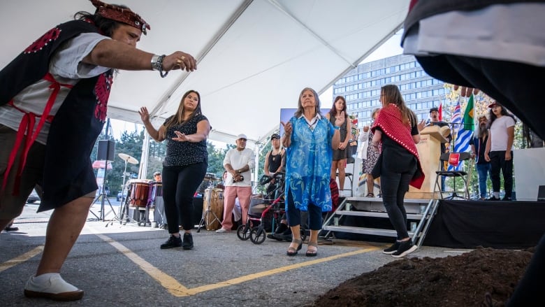 Indigenous people perform a ceremony by a pile of soil on top of pavement as part of a public event 