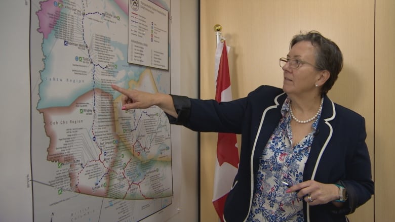 A woman wearing glasses and a dark blazer uses her right hand to point at a map.