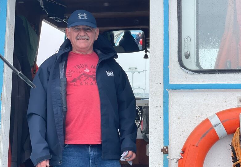 A man smiling and standing in the doorway of a fishing boat.