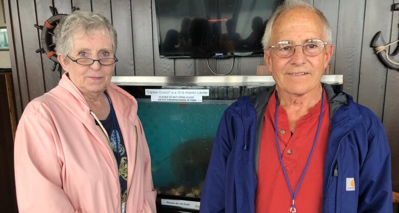 A woman and a man stand in front of a fish tank with an enormous lobster. 