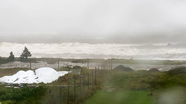 A rough sea with a farm in the foreground. There is water on the lens.