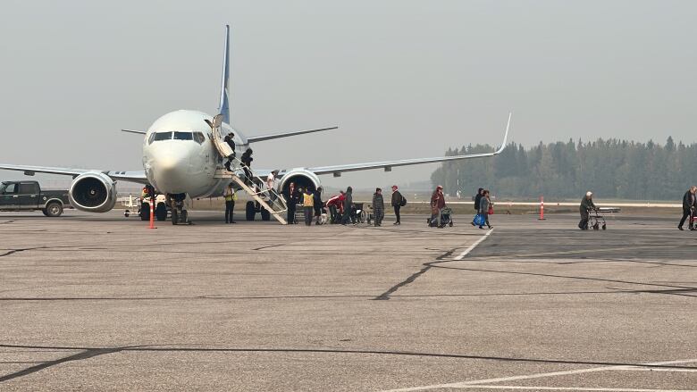 A plane on the ground with people disembarking.