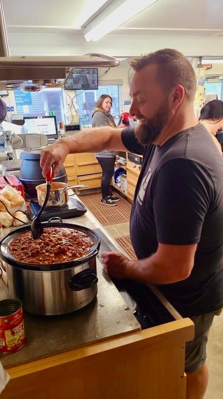 A man stirs a large crockpot full of chili.