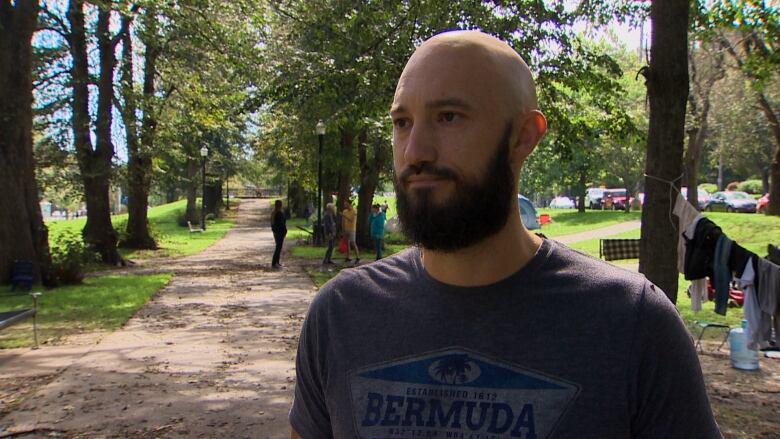 A bald man with a beard is shown in a Halifax park where there are many tents.