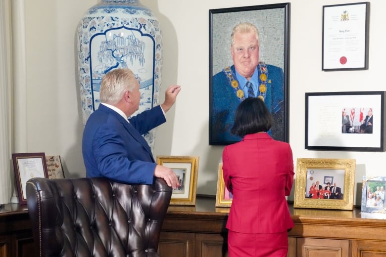 Two people look at photos on an office wall.