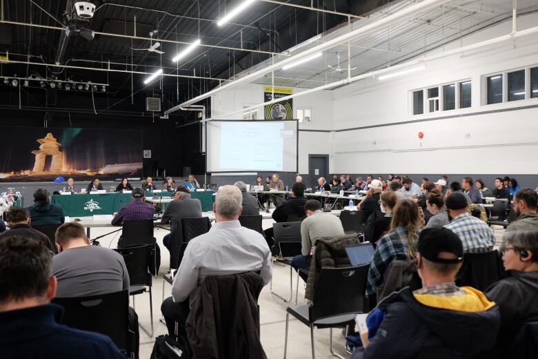 A hall full of people, with a panel of people at the front.