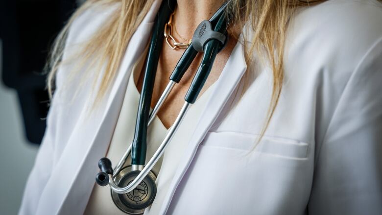 A doctor wears a lab coat and stethoscope in an exam room at a health clinic in Calgary, Friday, July 14, 2023.