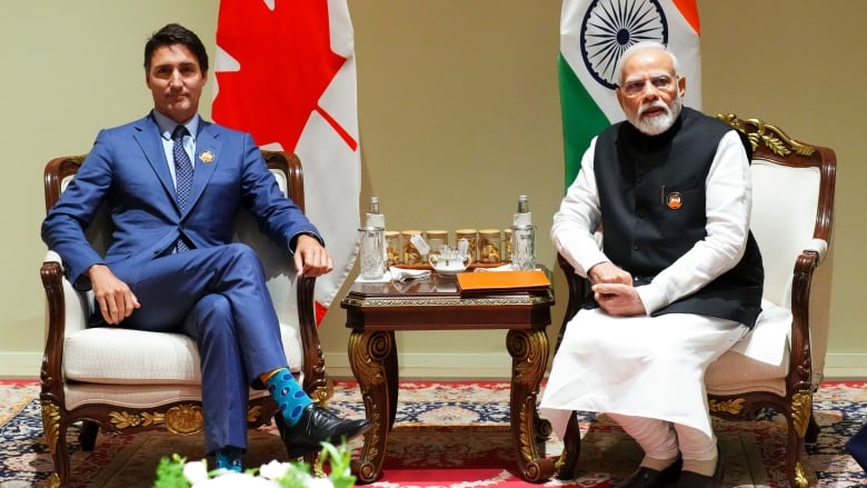 Two men sitting in ornate chairs, with flags of their respective countries behind them.