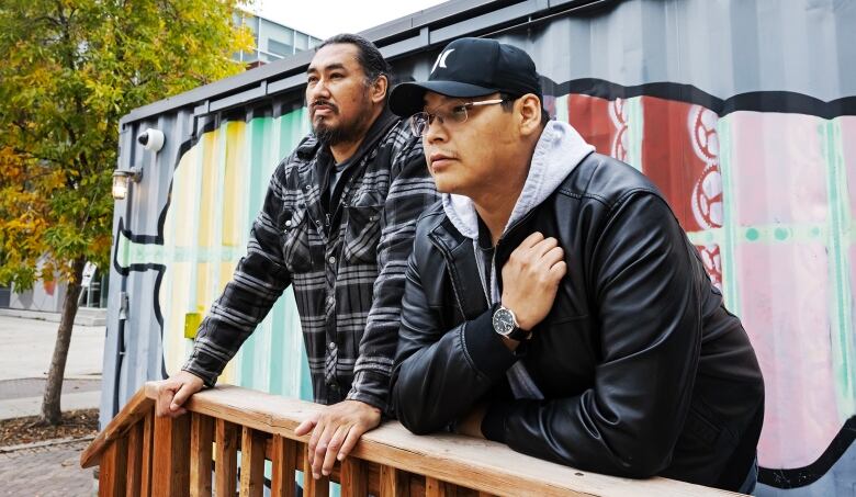 Two men leaning against a wood fence