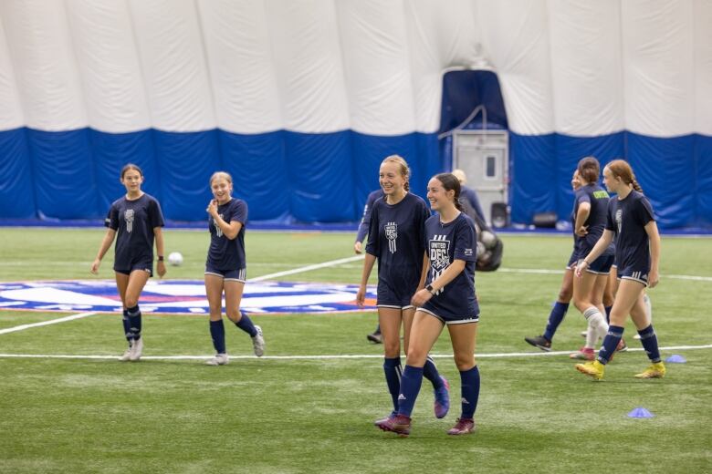 Female players are walking on the indoor field wearing blue uniforms.