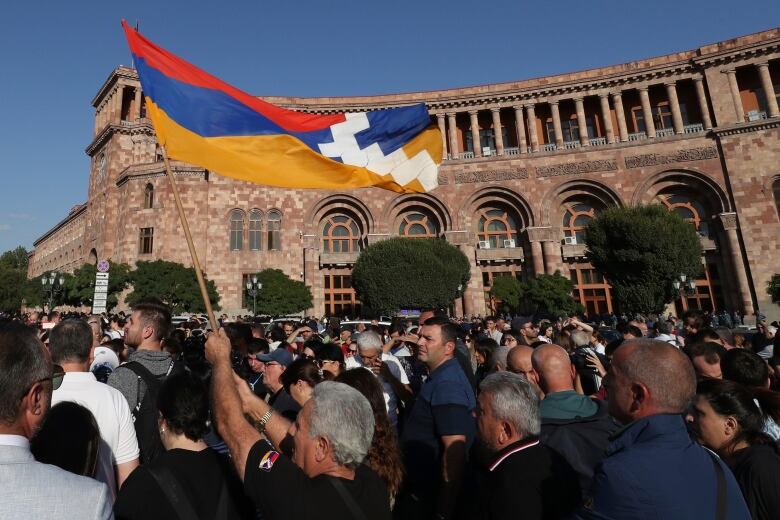 Dozens of people are shown on a street in a demonstration, with a giant flag being waved.