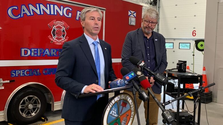 Two men stand in front of a fire truck.