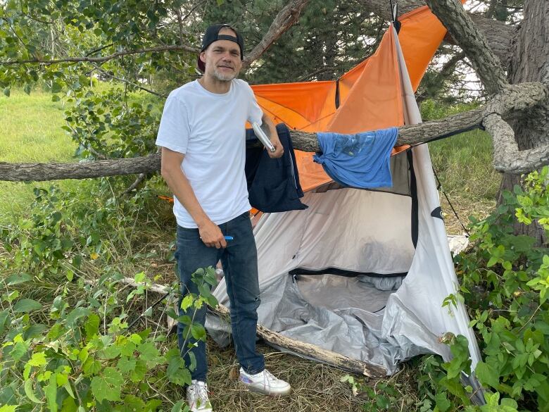 A man and a tent under a tree in a field in late summer.