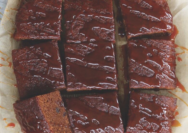 A sheet pan of cake is sliced into square sections. It is topped with a drizzle of caramel. 