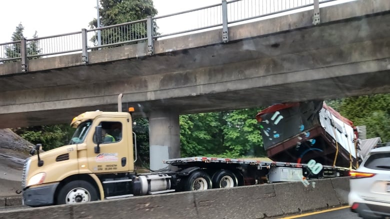 A truck which has just collided with an overpass is seen on a road, with a red payload behind it.