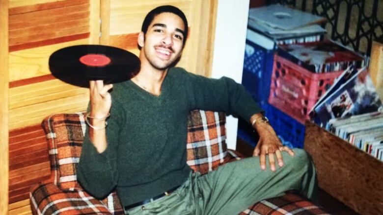 A teenager holds a vinyl record on his fingertip.