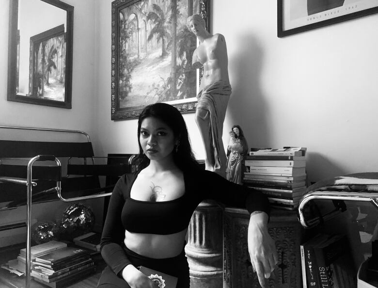 A black and white image of the author in an office corner with books, statues and paintings behind them