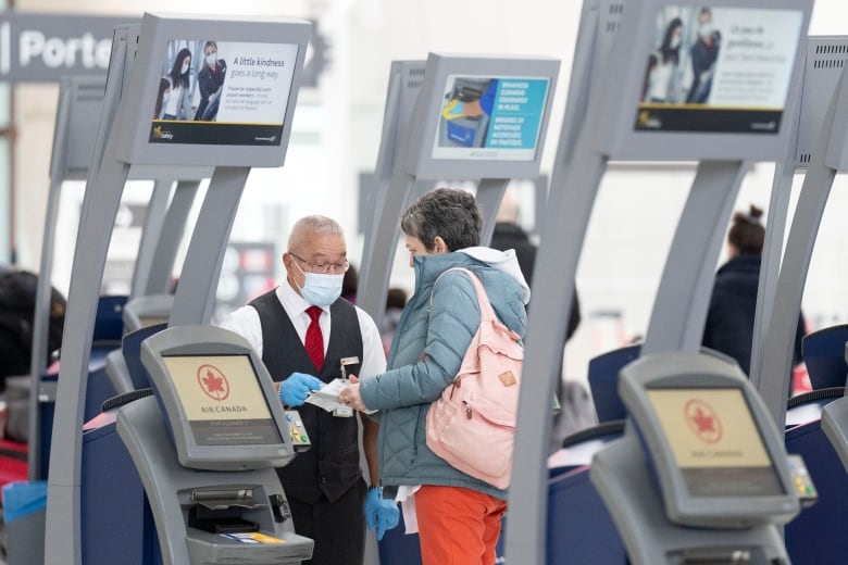 A traveller speaks with an airline employee beside self check-in kiosks.