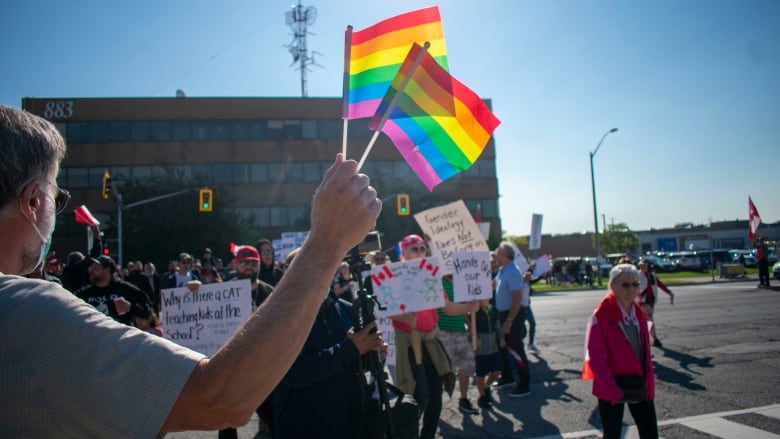 A person holding a rainbow flag and people in the background holding signs.