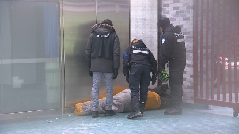 Police officers and a man stand over a person.