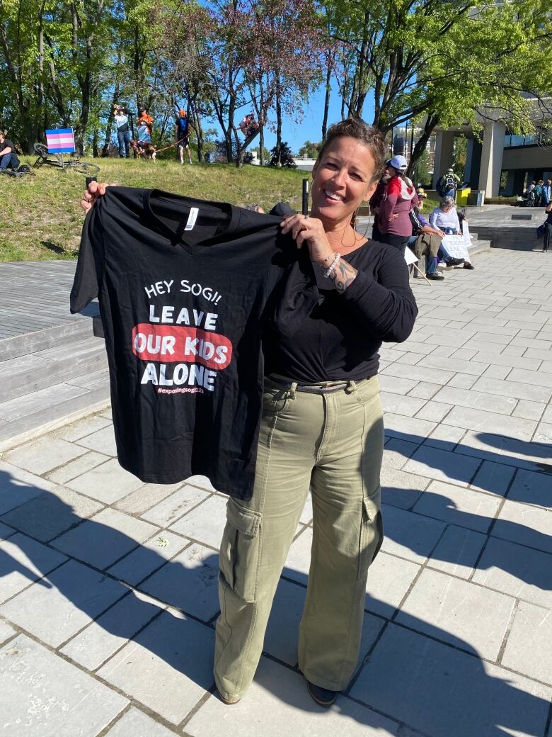 A woman holding a black shirt that says, 'Leave our kids alone.'