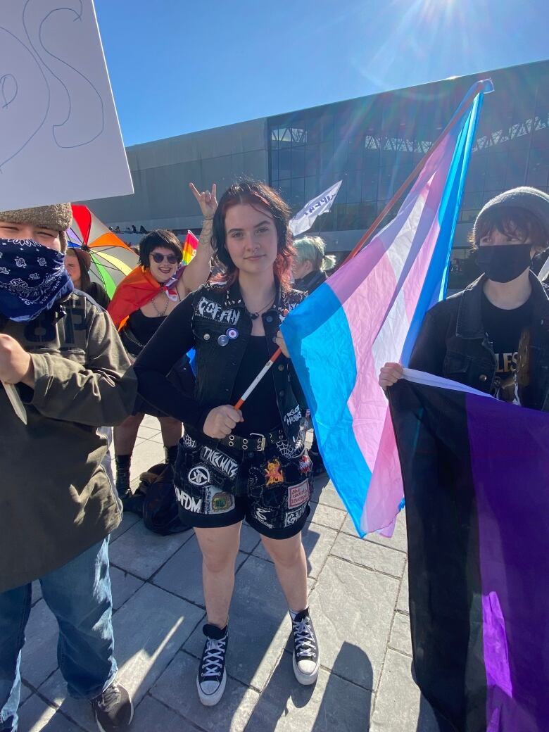 A young person dressed in black holding the trans flag.