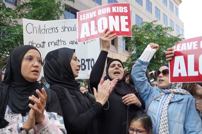 Women in headscarves carry signs saying 