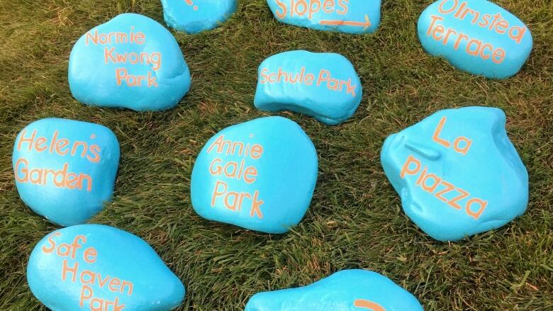 Blue painted rocks with orange text are arranged on a green lawn.