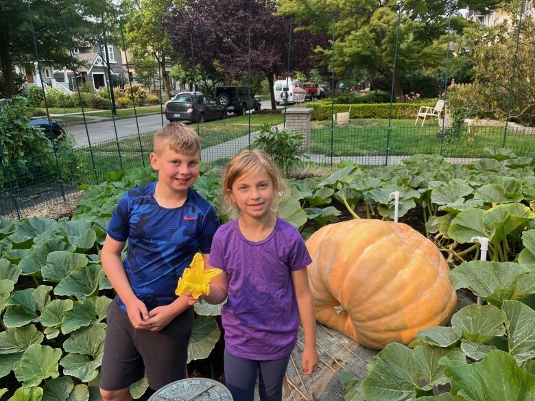 Two children, a boy and a girl pose in front of a giant pumpkin. 