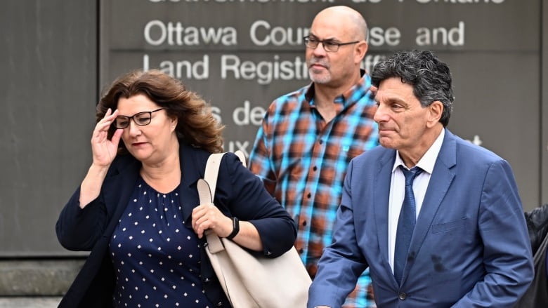 Three people walk past a sign for a provincial courthouse.