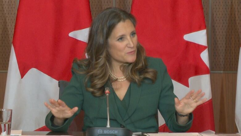 A woman wearing a green suit gestures with her hands.