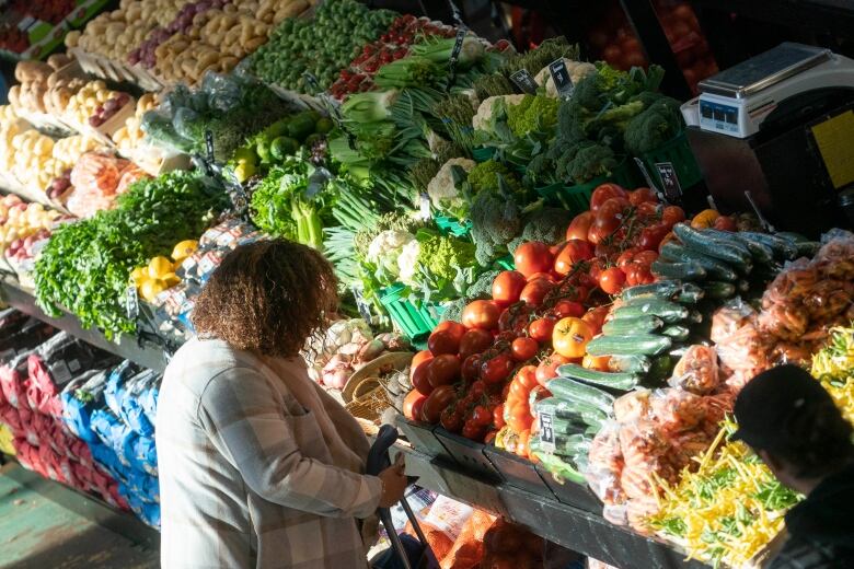 A woman stands in front of a market stall loaded with fresh vegetables. 