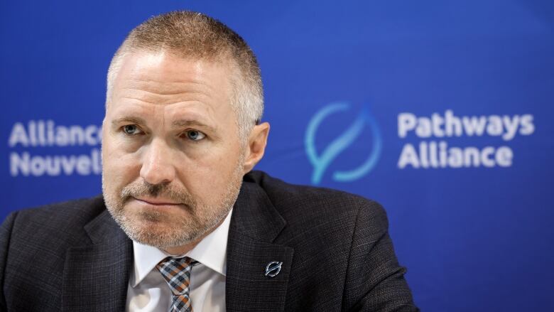 A man in a grey suit in front of a blue background