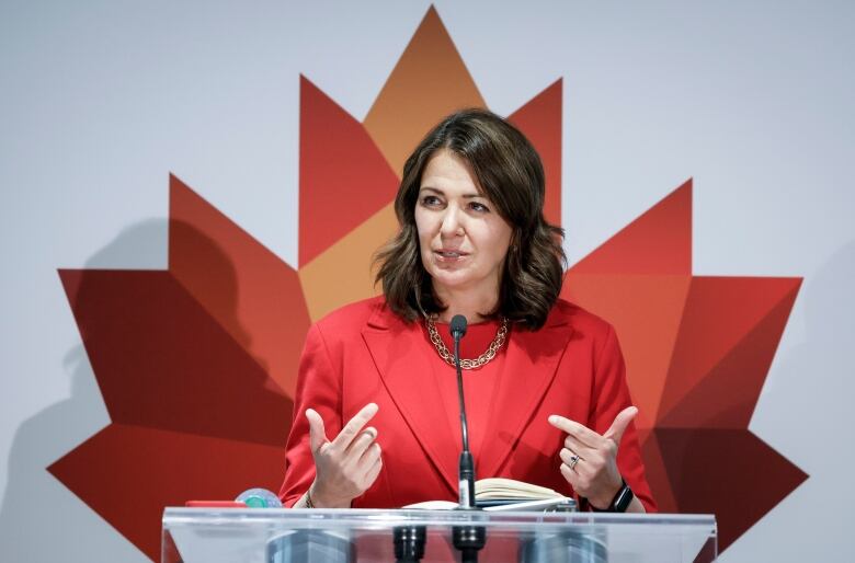 A woman in red speaks in front of a red maple leaf.