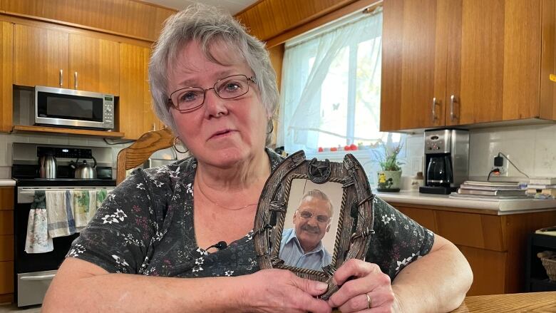 A woman with grey hair holds up a photo of a man.