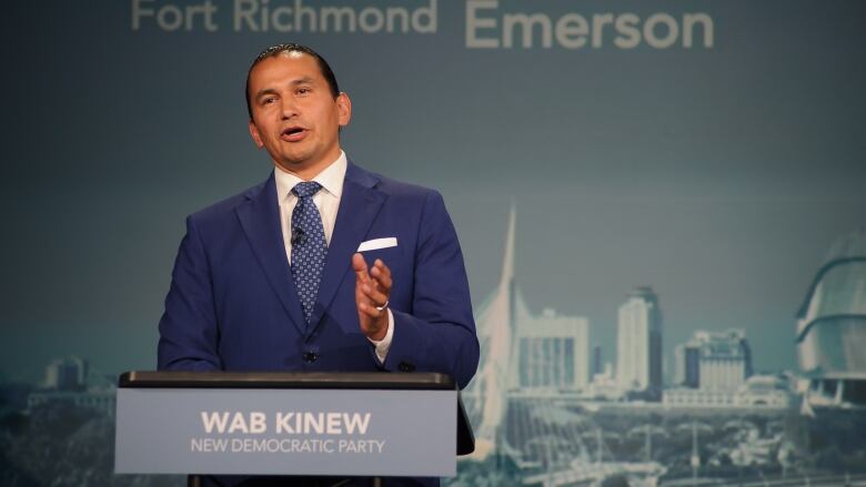 A man in a suit speaks at a podium.