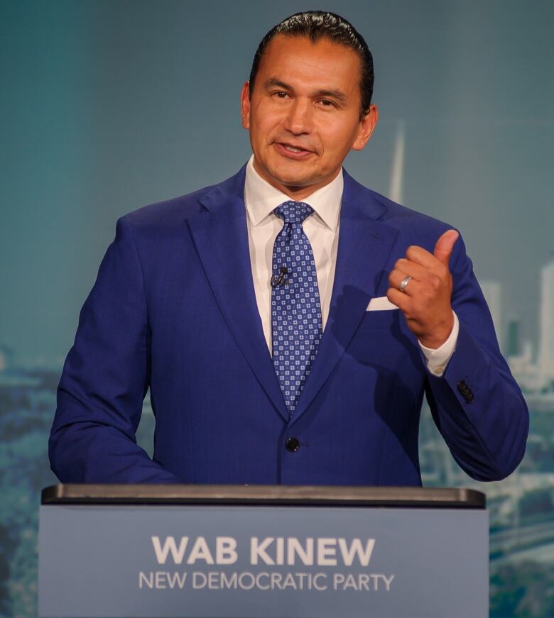 A man in a suit speaks at a podium.