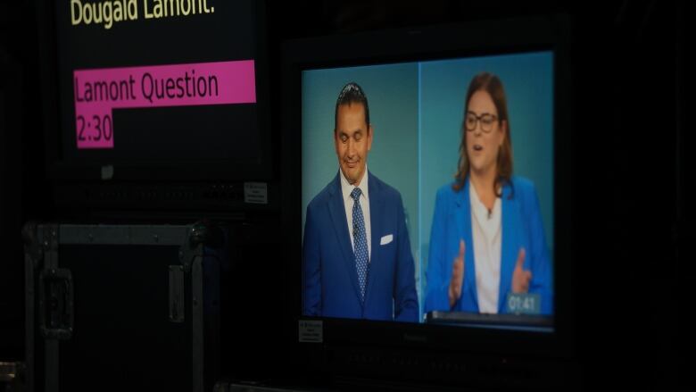 Two people in business attire are shown on the screen of a camera with prompter directions in the foreground.