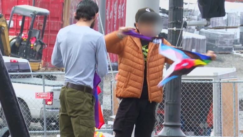 A person tearing apart rainbow flag, another person stands by