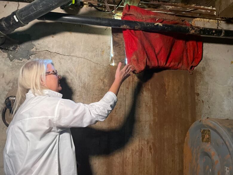 A woman pulls back a red cloth to reveal a window that's been boarded up, in a cement-walled basement.