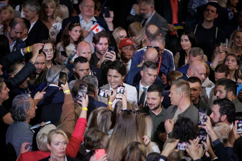 A crowd of people of with their phones out surround two men.