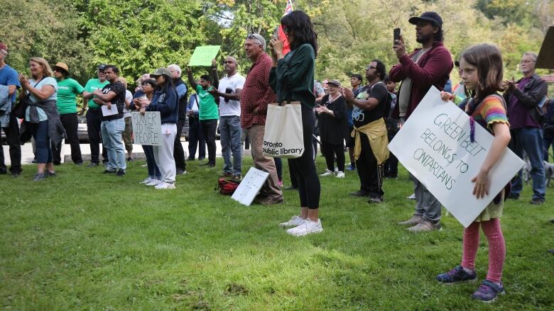 People standing in a park holding signs. 