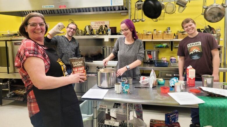 A group of four people are working to prepare meals in a commercial kitchen. The walls are a bright yellow.