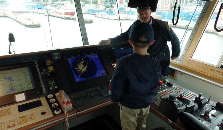 Man showing child the captain's station on a ship