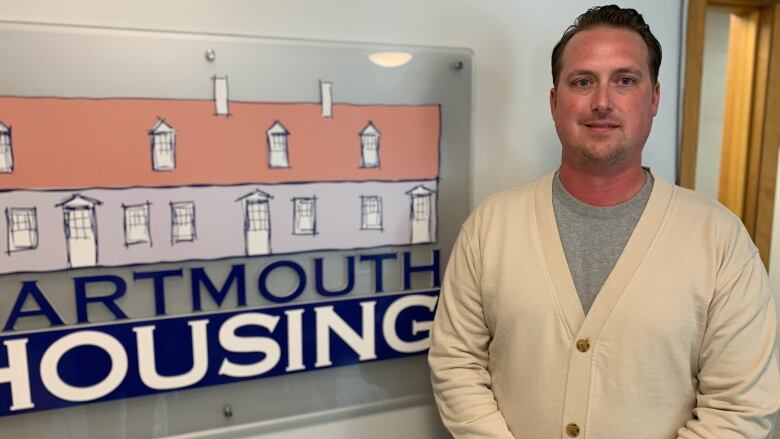 A man stands in an office in front of a sign reading 